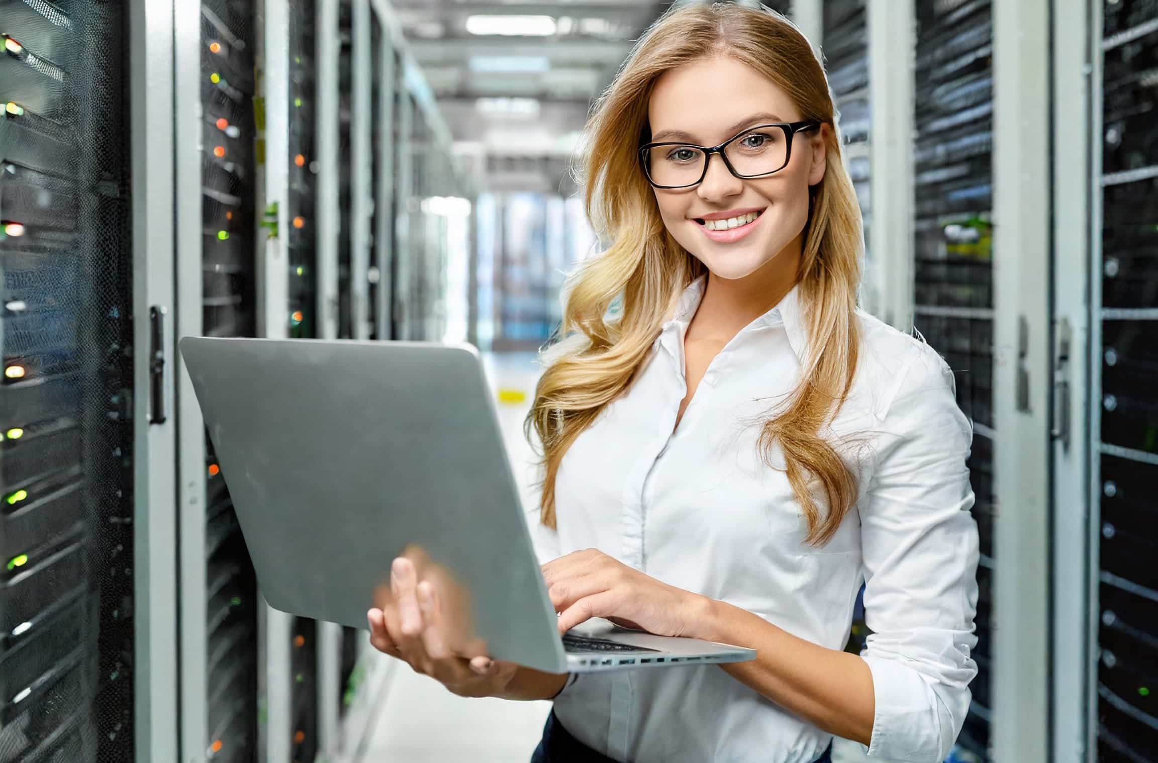 glückliche Frau am Laptop in einem Raum voller Serverschränke
